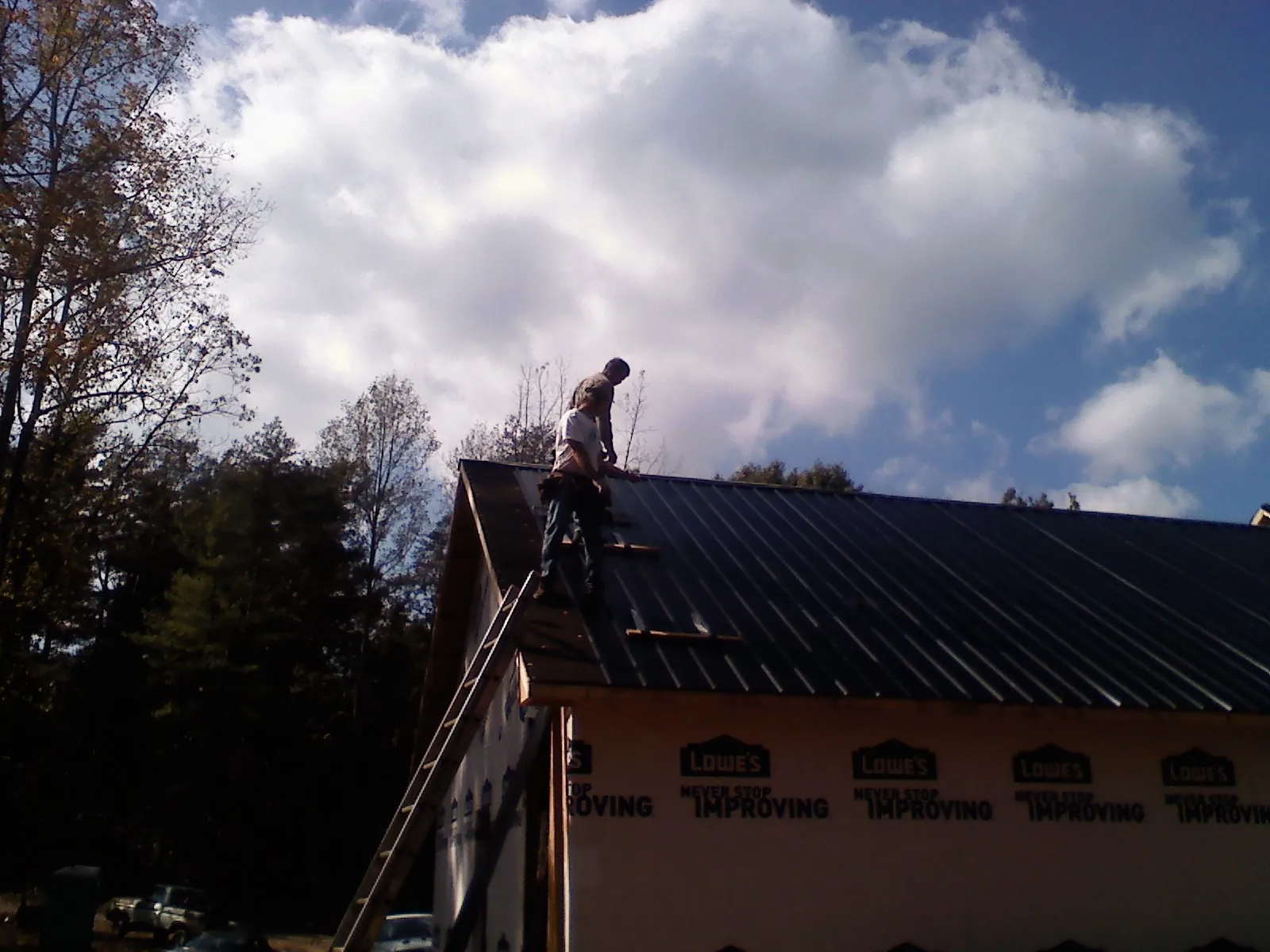Roofer fastening dark metal panels high against a cloudy sky, from a Roof Inspection job in Camden